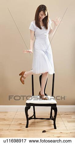 Stock Photo - Young woman standing on chair, evading mouse. Fotosearch