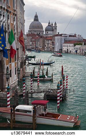 Stock Image - Aerial view of Grand Canal, looking towards church of Santa Maria della Salute, multicoloured flags and striped mooring posts, Venice, Northern Italy. Fotosearch