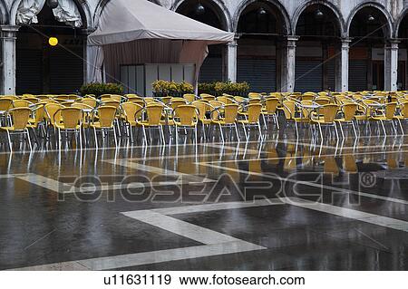 Aqua Alta flooding in Piazza San Marco: desaturated image highlighting empty yellow chairs, and grey facade and loggia of the Procuratie behind, reflected in the water, Venice, Northern Italy View Large Photo Image Stock Photo - Aqua Alta flooding in Piazza San Marco: desaturated image highlighting empty yellow chairs, and grey facade and loggia of the Procuratie behind, reflected in the water, Venice, Northern Italy. Fotosearch