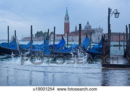Aqua Alta: view of San Marco basin, looking past moored gondolas with motion blur of rough water and flooding in foreground, to San Giorgio Maggiore church and nearby harbour, autumn in Venice, Northern Italy View Large Photo Image Picture - Aqua Alta: view of San Marco basin, looking past moored gondolas with motion blur of rough water and flooding in foreground, to San Giorgio Maggiore church and nearby harbour, autumn in Venice, Northern Italy. Fotosearch