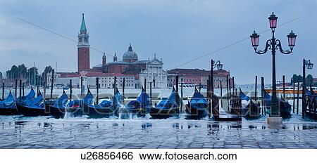 Stock Photograph - Aqua Alta: view of San Marco basin, looking past moored gondolas with motion blur of rough water and flooding in foreground, to San Giorgio Maggiore church and nearby harbour, autumn in Venice, Northern Italy. Fotosearch
