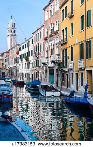 Stock Image - Boats moored alongside canal with reflections of palace buildings in water, and Romanesque bell tower in distance, sunny autumn morning in Venice, Northern Italy. Fotosearch
