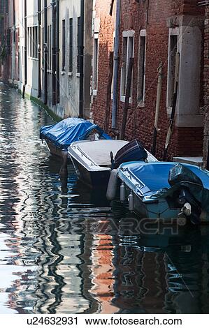 Boats moored alongside canal with reflections of palace buildings in water, sunny autumn morning in Venice, Northern Italy View Large Photo Image Stock Image - Boats moored alongside canal with reflections of palace buildings in water, sunny autumn morning in Venice, Northern Italy. Fotosearch