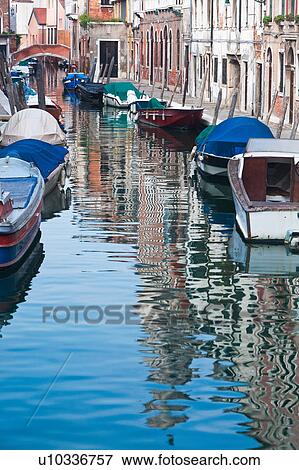Stock Photo - Boats moored alongside canal with reflections of palace buildings in water, sunny autumn morning in Venice, Northern Italy. Fotosearch