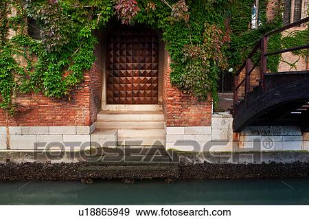 Canal-side doorway to home, with wooden door, and ivy trailing across red brick wall, wooden bridge across canal, Venice, Northern Italy View Large Photo Image Stock Photo - Canal-side doorway to home, with wooden door, and ivy trailing across red brick wall, wooden bridge across canal, Venice, Northern Italy. Fotosearch