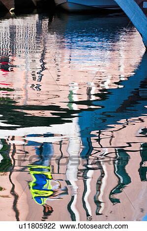 Stock Image - Close up of canal reflection: arch of bridge with man walking across, wearing brightly coloured work jacket, sunny autumn morning in Venice, Northern Italy. Fotosearch