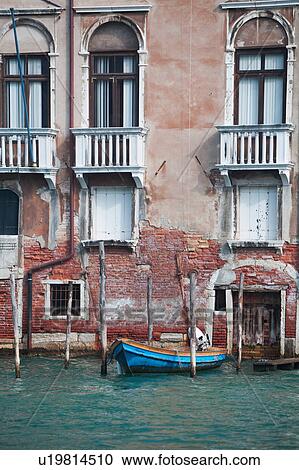Stock Image - Crumbling Renaissance facade of palace beside canal, with old wooden boat moored, sunny autumn morning in Venice, Northern Italy. Fotosearch