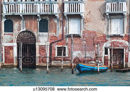 Stock Photo - Crumbling Renaissance facade of palace beside canal, with old wooden boat moored, sunny autumn morning in Venice, Northern Italy. Fotosearch
