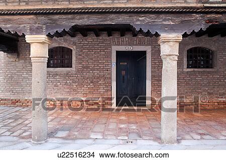 Picture - Detail of red brick medieval palace with loggia over doorway supported by stone columns and wooden beams, in late afternoon sunlight, autumn in Venice, Northern Italy. Fotosearch