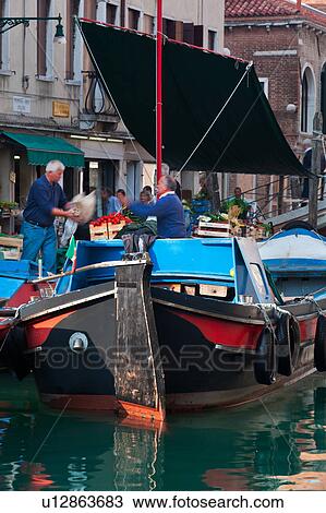 Fruit and vegetable market on colourful blue and red barge with motion blur of vendor and shoppers, with men loading produce, sunny autumn morning in Venice, Northern Italy View Large Photo Image Stock Image - Fruit and vegetable market on colourful blue and red barge with motion blur of vendor and shoppers, with men loading produce, sunny autumn morning in Venice, Northern Italy. Fotosearch