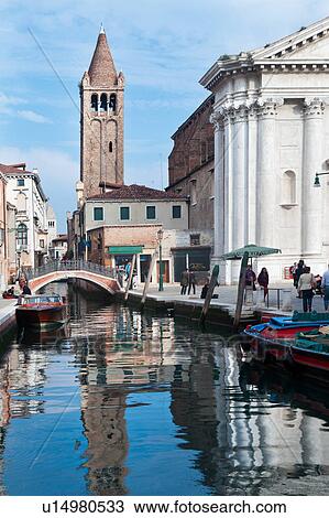 Motorboat and barge moored alongside canal with reflections of Renaissance church and Romanesque bell tower in water, people wandering in piazza, sunny autumn morning in Venice, Northern Italy View Large Photo Image Stock Image - Motorboat and barge moored alongside canal with reflections of Renaissance church and Romanesque bell tower in water, people wandering in piazza, sunny autumn morning in Venice, Northern Italy. Fotosearch