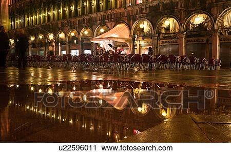 Piazza San Marco at night, with Aqua Alta flooding, lights of loggia reflected in puddles, rows of empty red and yellow chairs, orchestra with grand piano, and motion blur of few passersby, Venice, Northern Italy View Large Photo Image Stock Image - Piazza San Marco at night, with Aqua Alta flooding, lights of loggia reflected in puddles, rows of empty red and yellow chairs, orchestra with grand piano, and motion blur of few passersby, Venice, Northern Italy. Fotosearch