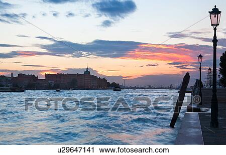 Stock Image - View of Canale della Giudecca, looking towards Stucky Mill, and harbour with tall ship, at sunset, autumn in Venice, Northern Italy. Fotosearch
