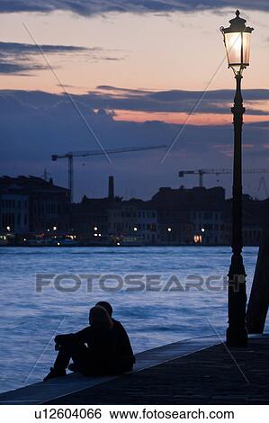 View of Canale della Giudecca, with young couple silhouetted, sitting beside illuminated wrought iron lamp on quayside, looking towards Giudecca, twilight, autumn in Venice, Northern Italy View Large Photo Image Stock Photograph - View of Canale della Giudecca, with young couple silhouetted, sitting beside illuminated wrought iron lamp on quayside, looking towards Giudecca, twilight, autumn in Venice, Northern Italy. Fotosearch