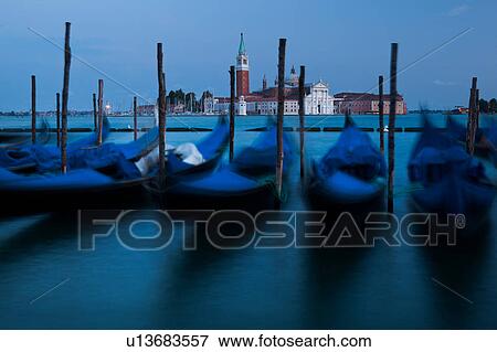 View of San Marco basin, looking past moored gondolas with motion blur in foreground, to San Giorgio Maggiore church and nearby harbour, dusk with lighthouse shining, autumn in Venice, Northern Italy View Large Photo Image Stock Photo - View of San Marco basin, looking past moored gondolas with motion blur in foreground, to San Giorgio Maggiore church and nearby harbour, dusk with lighthouse shining, autumn in Venice, Northern Italy. Fotosearch