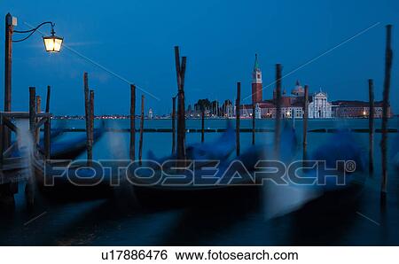 View of San Marco basin, looking past moored gondolas with motion blur in foreground, to San Giorgio Maggiore church and nearby harbour, dusk with lighthouse shining, lights of Giudecca, autumn in Venice, Northern Italy View Large Photo Image Stock Photograph - View of San Marco basin, looking past moored gondolas with motion blur in foreground, to San Giorgio Maggiore church and nearby harbour, dusk with lighthouse shining, lights of Giudecca, autumn in Venice, Northern Italy. Fotosearch