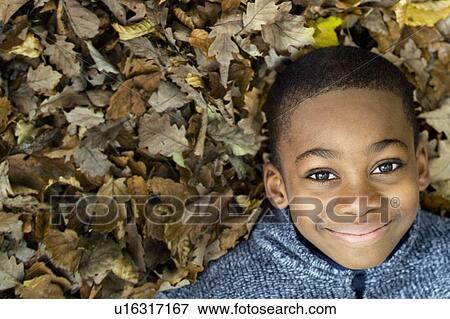 Stock Photo - Smiling boy lying on autumn leaves. Fotosearch