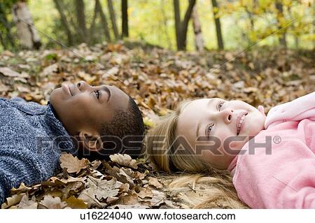 Stock Image - Smiling children lying on autumn leaves. Fotosearch