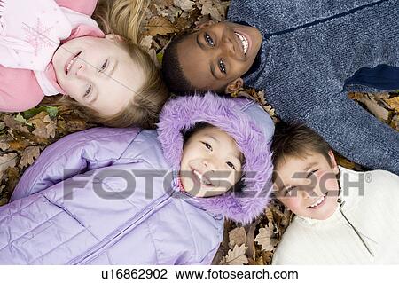 Stock Image - Smiling children lying on autumn leaves. Fotosearch
