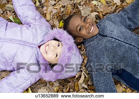 Smiling children lying on autumn leaves View Large Photo Image Stock Photo - Smiling children lying on autumn leaves. Fotosearch