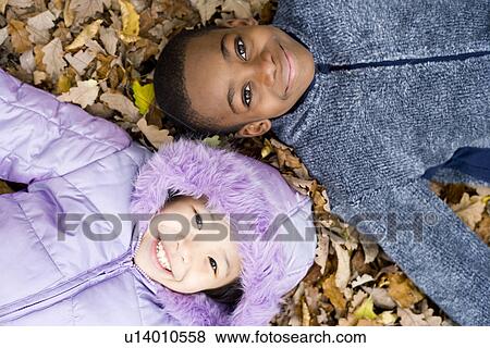 Stock Photo - Smiling children lying on autumn leaves. Fotosearch