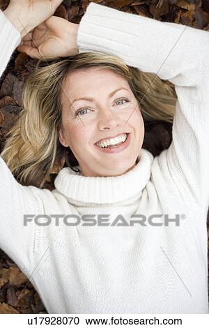 Stock Image - Smiling woman lying on autumn leaves. Fotosearch