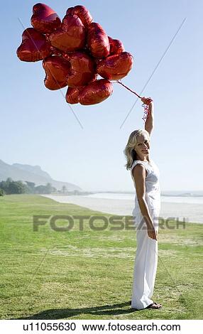 Stock Image - Woman holding heart-shaped balloons. Fotosearch