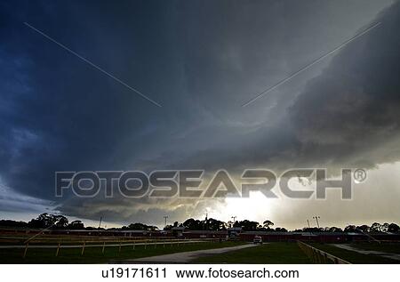 Stock Image - A storm with a shelf cloud and the sun shining through, the rain sweeping over Port St. John, Florida. Fotosearch