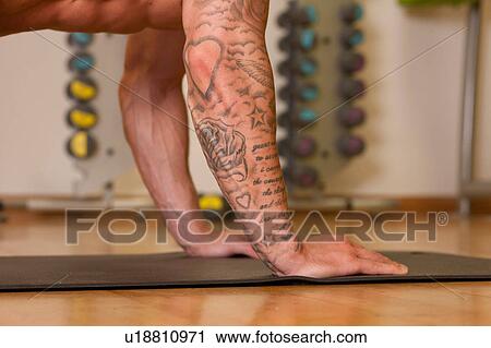 Stock Image - Arms of tattooed man exercising on yoga mat in gym. Fotosearch