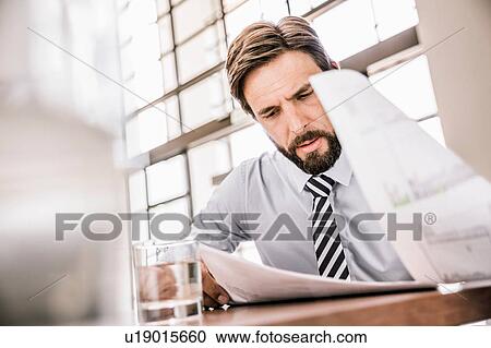 Stock Image - Bearded businessman looking down at paperwork. Fotosearch