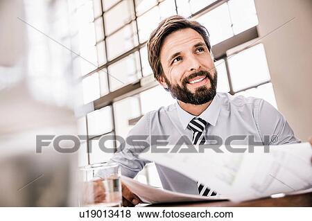 Stock Photo - Bearded businessman with paperwork looking away smiling. Fotosearch