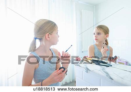 Stock Image - Bedroom mirror image of girl with make up brush staring at herself. Fotosearch