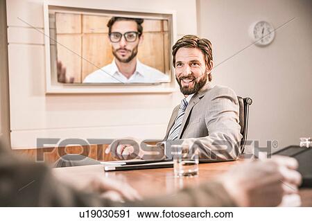 Stock Image - Business people in boardroom having video call meeting. Fotosearch