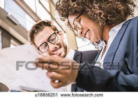 Stock Image - Businessman and businesswoman reading paperwork outside office. Fotosearch