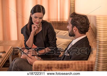 Stock Image - Businessman and woman sitting on hotel sofa using digital tablet. Fotosearch
