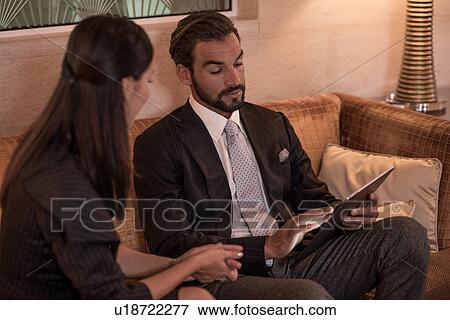 Businessman and woman sitting on hotel sofa looking at digital tablet View Large Photo Image Stock Photo - Businessman and woman sitting on hotel sofa looking at digital tablet. Fotosearch