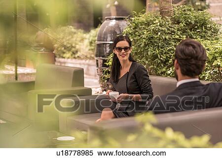 Stock Photography - Businessman and woman talking on hotel garden sofa, Dubai, United Arab Emirates. Fotosearch