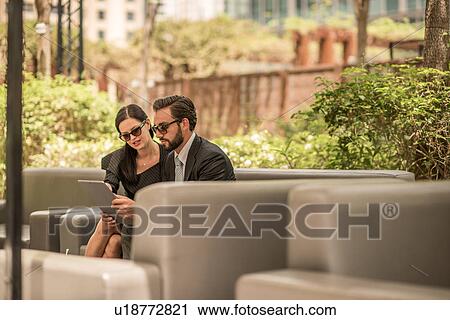 Businessman and woman using digital tablet on hotel garden sofa, Dubai, United Arab Emirates View Large Photo Image Stock Image - Businessman and woman using digital tablet on hotel garden sofa, Dubai, United Arab Emirates. Fotosearch
