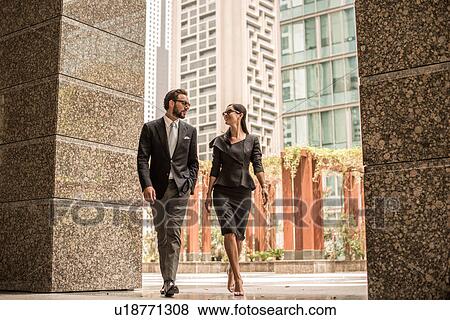 Stock Photo - Businessman and woman walking and talking outside office, Dubai, United Arab Emirates. Fotosearch
