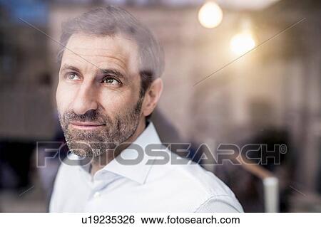 Businessman gazing up through office window View Large Photo Image Stock Photograph - Businessman gazing up through office window. Fotosearch