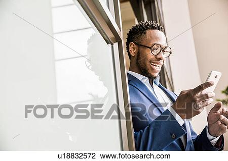 Stock Image - Businessman in office doorway reading smartphone text. Fotosearch
