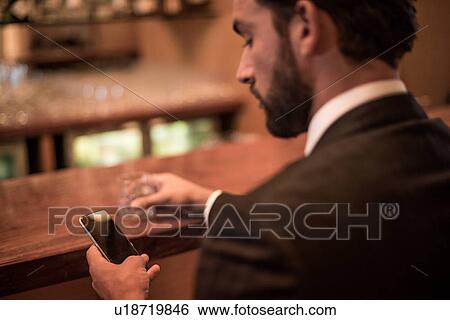 Businessman reading smartphone text at hotel bar View Large Photo Image Stock Photograph - Businessman reading smartphone text at hotel bar. Fotosearch