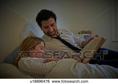 Stock Photo - Businessman reading storybook to sleeping daughter at bedtime. Fotosearch