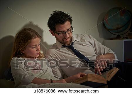 Stock Photograph - Businessman reading storybook to daughter at bedtime. Fotosearch