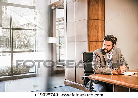 Businessman sitting at desk looking away View Large Photo Image Stock Photo - Businessman sitting at desk looking away. Fotosearch