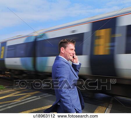 Businessman standing at level crossing, using smartphone View Large Photo Image Stock Image - Businessman standing at level crossing, using smartphone. Fotosearch