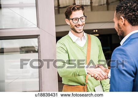 Stock Image - Businessmen shaking hands outside office building. Fotosearch