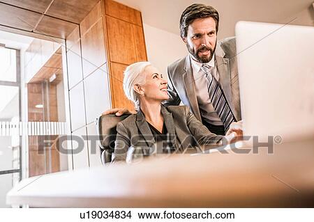 Businesspeople at desk looking at laptop smiling View Large Photo Image Picture - Businesspeople at desk looking at laptop smiling. Fotosearch