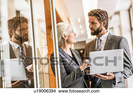 Picture - Businesspeople wearing suits holding laptop face to face smiling. Fotosearch