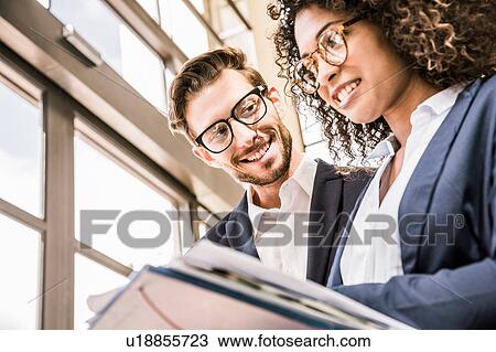Stock Image - Businesswoman and businessman reading paperwork outside office. Fotosearch